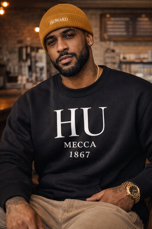 Man wearing a black sweatshirt with 'HU Mecca 1867' text, sitting in a bar setting.